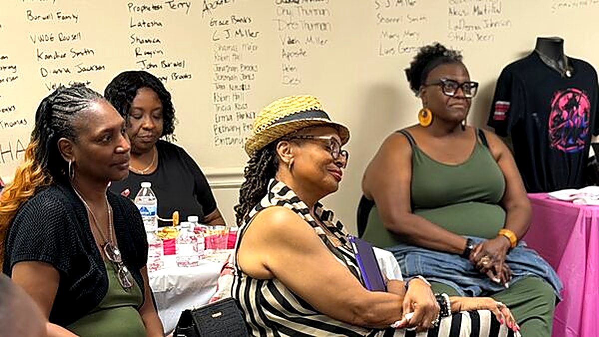 Women of every generation seated together beneath the wall of names