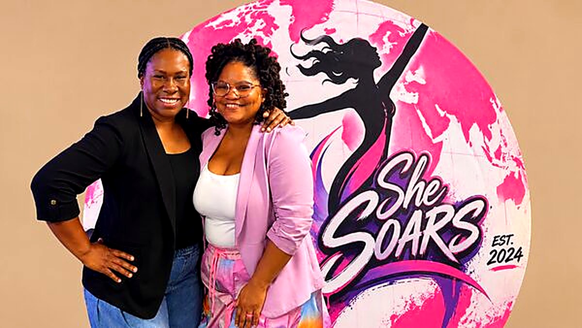 Two sisters embracing at the She SOARS backdrop