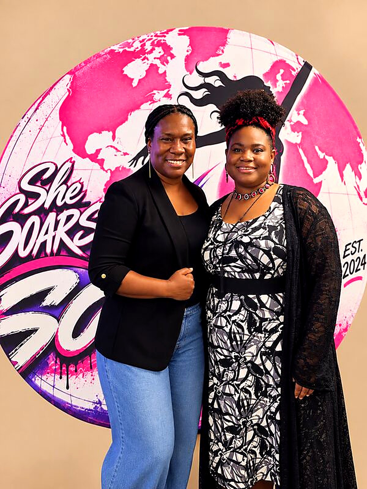 Two sisters smiling together at the She SOARS backdrop